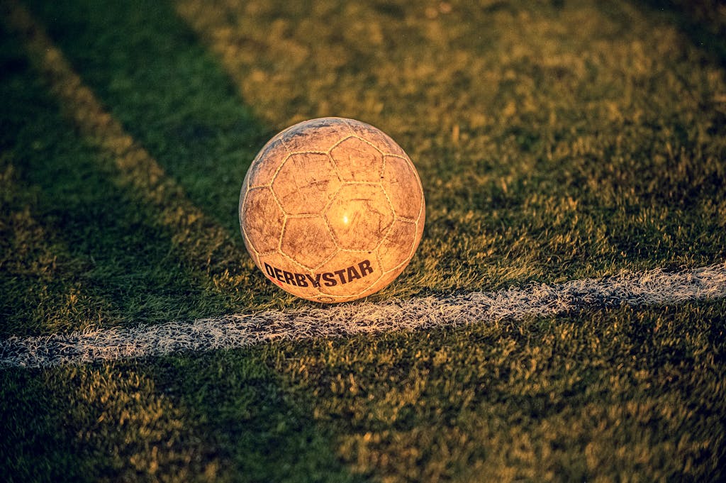 Close-up of a worn soccer ball on a grassy field during sunset, capturing the essence of play.